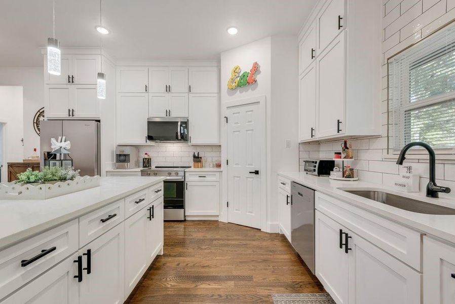 Kitchen with stainless steel appliances, white cabinetry, hanging light fixtures, and dark wood-style flooring