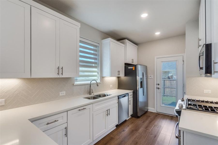 Kitchen with tasteful backsplash, white cabinetry, dark wood-style flooring, stainless steel appliances, and recessed lighting Kitchen with tasteful backsplash, white cabinetry, dark wood-style flooring, stainless steel appliances, and recessed lighting