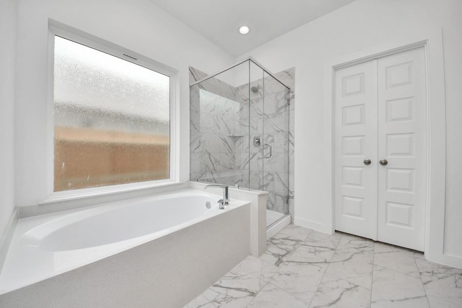 Escape to a spa-like oasis in this primary bathroom. Enjoy a walk-in shower with tile surround, a separate garden tub with custom detailing, and an elegant vanity featuring light countertops, modern hardware, and beautiful recessed lights. Experience luxury and relaxation in every detail. Sample photo of completed home with similar floor plan. Actual colors and selections may vary.