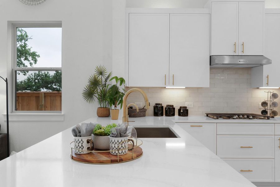 Kitchen with under cabinet range hood, stainless steel gas cooktop, a sink, white cabinets, and tasteful backsplash Kitchen with under cabinet range hood, stainless steel gas cooktop, a sink, white cabinets, and tasteful backsplash