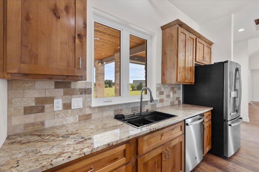 Kitchen featuring stainless steel appliances, wood finished floors, light stone counters, tasteful backsplash, and brown cabinets