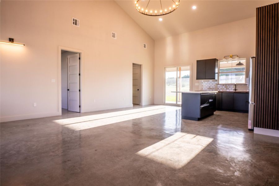 Unfurnished living room with concrete floors, a chandelier, high vaulted ceiling, and recessed lighting