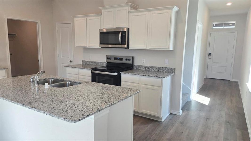 Kitchen featuring stainless steel appliances, white cabinetry, light stone counters, and a center island with sink