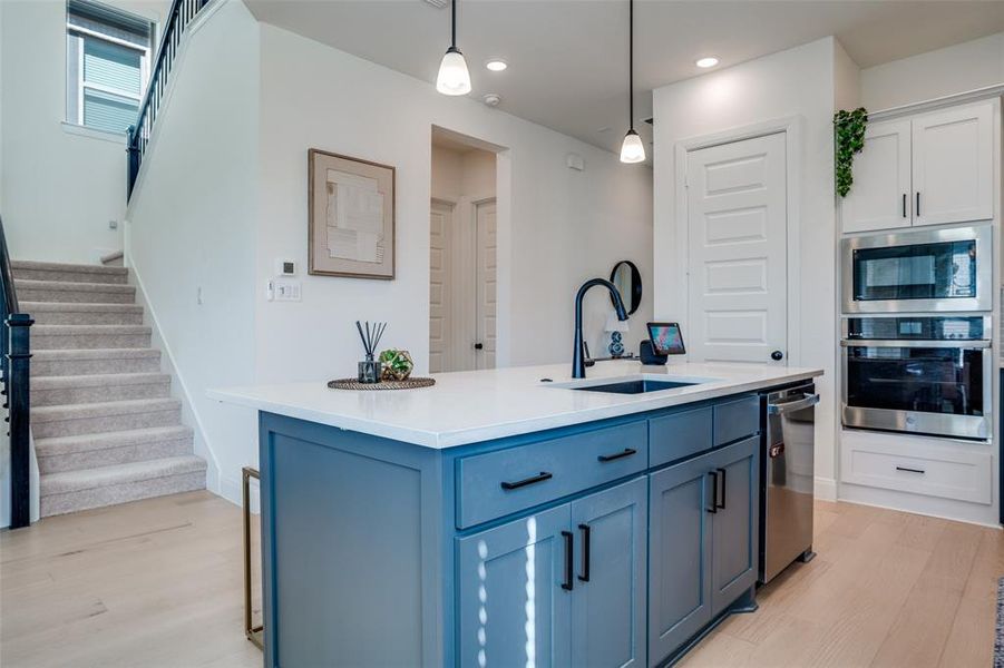 Kitchen with stainless steel appliances, light wood-style flooring, pendant lighting, light stone counters, and two tone cabinets