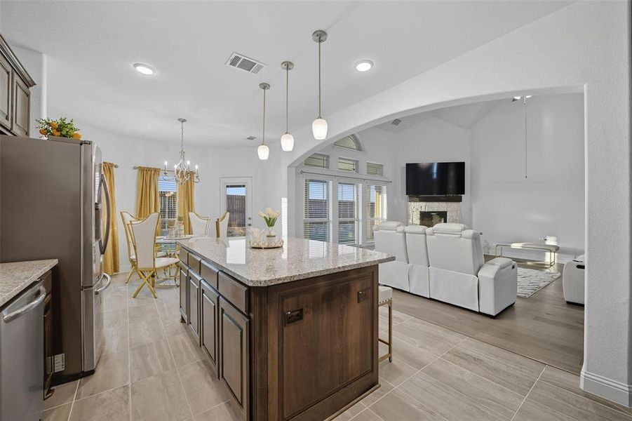 Kitchen with dark brown cabinetry, pendant lighting, light stone countertops, stainless steel appliances, and healthy amount of natural light Kitchen with dark brown cabinetry, pendant lighting, light stone countertops, stainless steel appliances, and healthy amount of natural light