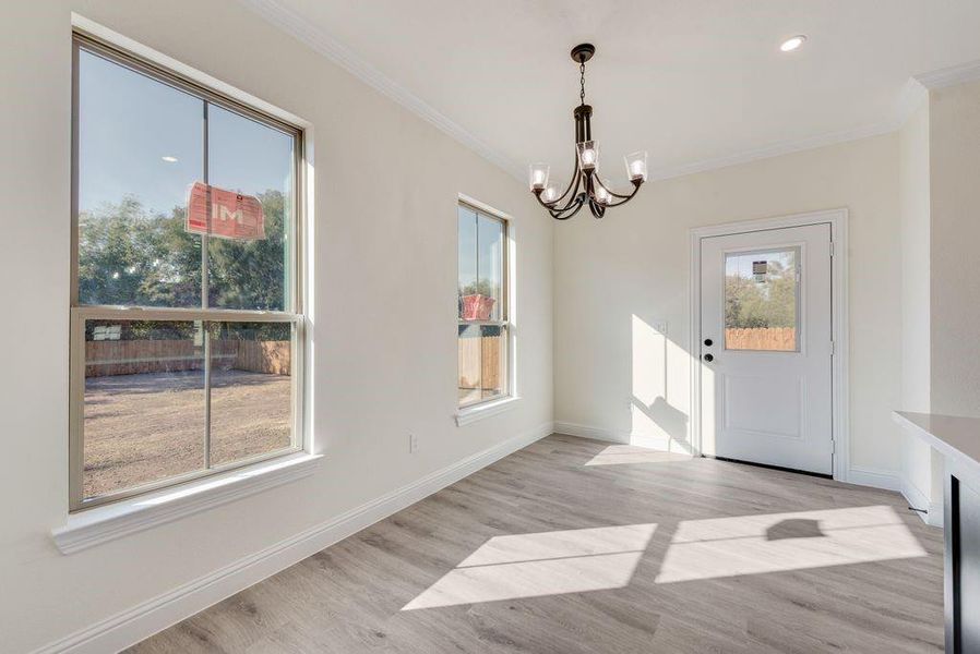 Unfurnished dining area with light hardwood / wood-style floors, crown molding, a healthy amount of sunlight, and a chandelier