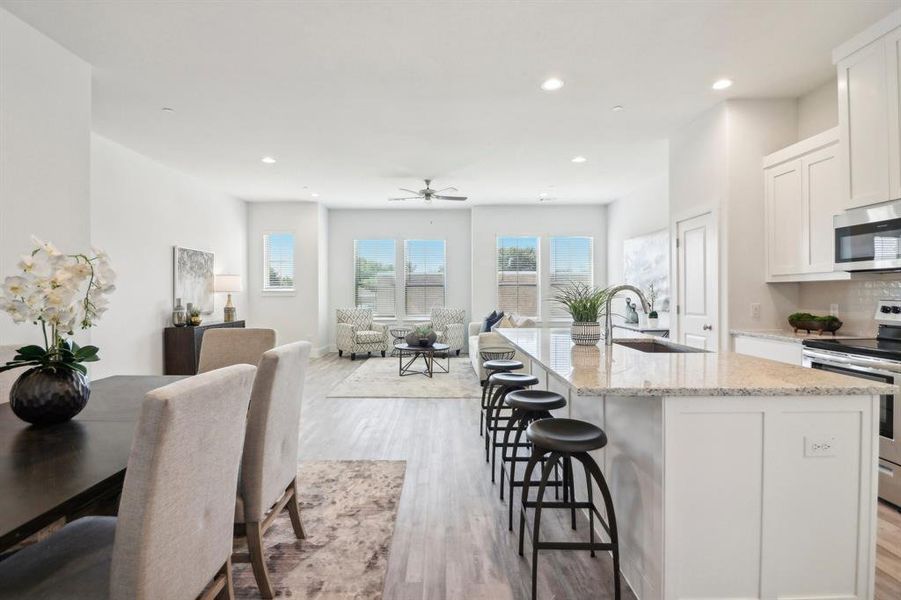 Kitchen with a kitchen island with sink, white cabinets, light wood-type flooring, appliances with stainless steel finishes, and light stone counters