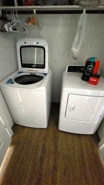 Dedicated laundry area featuring a white top-load washing machine, a white front-load dryer, wood-finish flooring, and an upper storage shelf