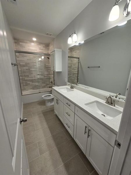 Full bathroom with toilet, bath / shower combo with glass door, double sink vanity, and tile patterned flooring