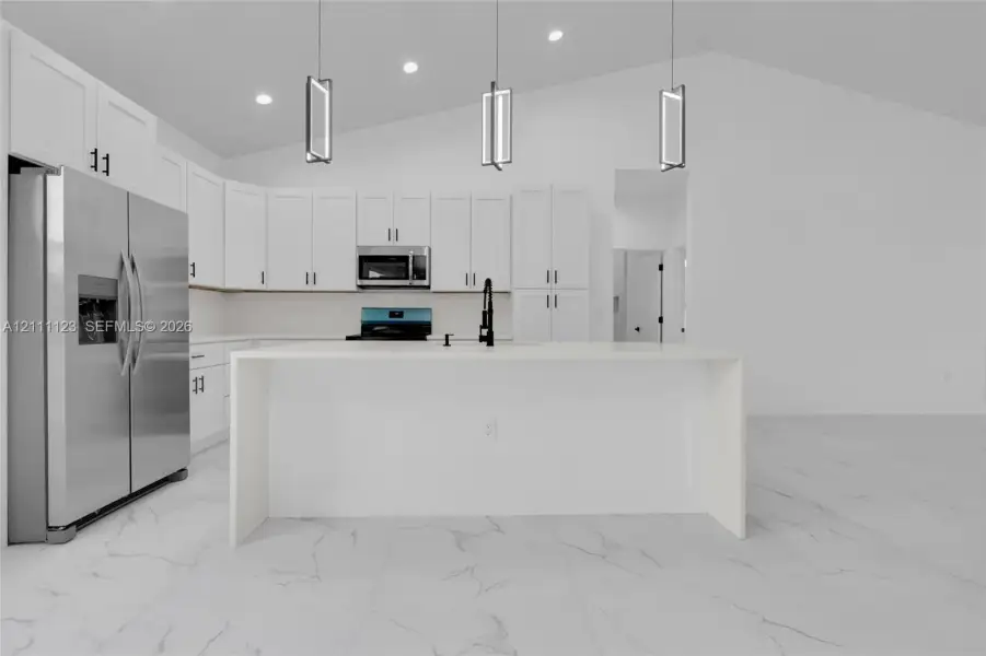 Large waterfall-edge quartz island with stainless steel refrigerator and full-height backsplash.
