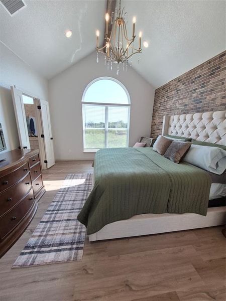 Bedroom with vaulted ceiling, brick wall, wood finished floors, a textured ceiling, and a chandelier