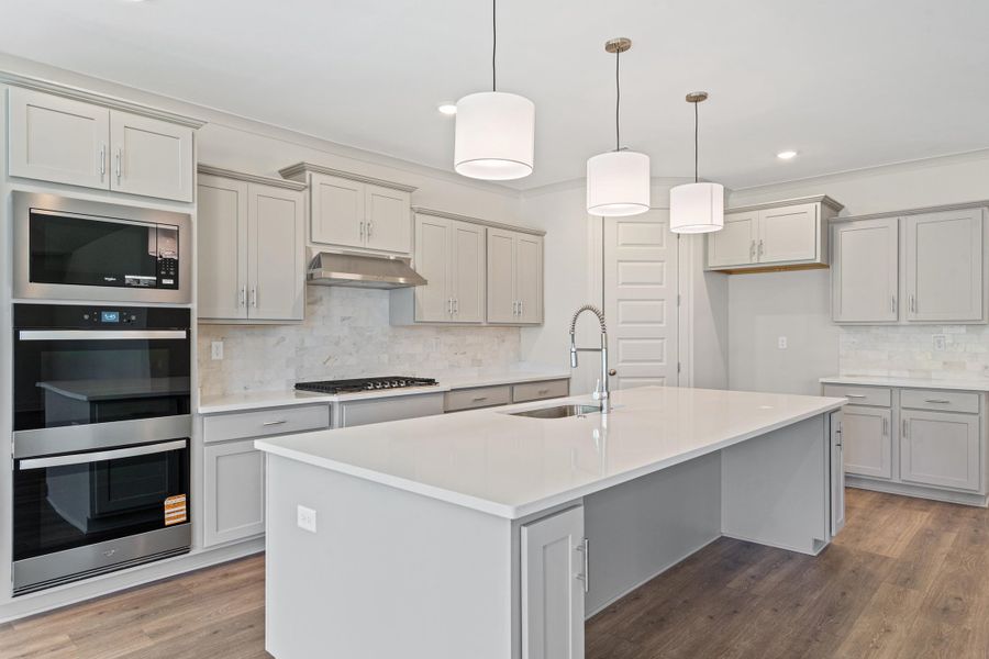 Kitchen with stainless steel appliances, gray cabinets, light wood-style flooring, a center island with sink, and crown molding