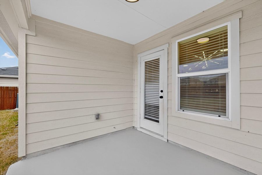 A covered back porch features neutral siding, a concrete floor, and glass-paneled entry door.