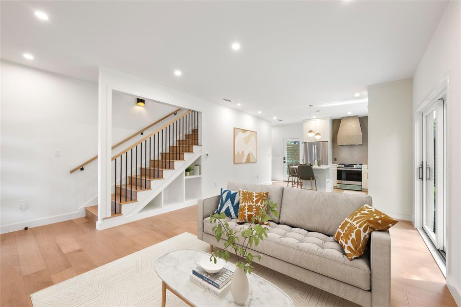 Blonde hardwood floors extend throughout an open-concept living area and kitchen, featuring a striking contemporary staircase. Blonde hardwood floors extend throughout an open-concept living area and kitchen, featuring a striking contemporary staircase.