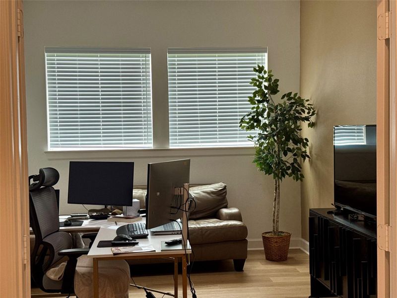 Bright home office space featuring large windows with blinds, a comfortable seating area, and ample room for workstations.