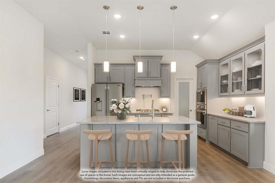 Kitchen with gray cabinets, large island with three bar stools, pendant lights, and stainless steel appliances on wood floors Kitchen with gray cabinets, large island with three bar stools, pendant lights, and stainless steel appliances on wood floors