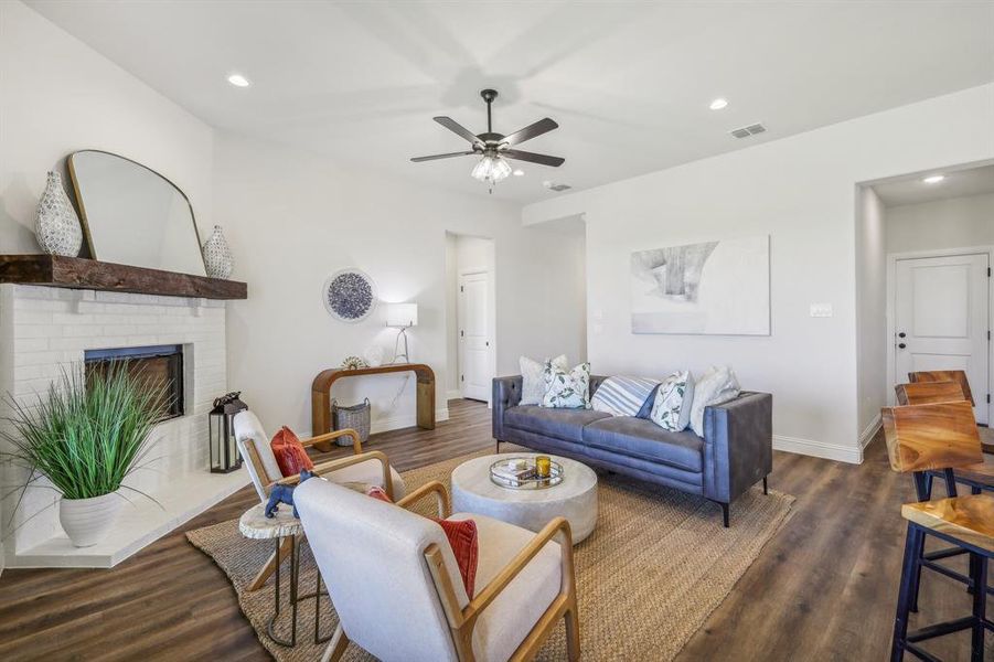 Living room with a brick fireplace, ceiling fan, and dark wood-type flooring