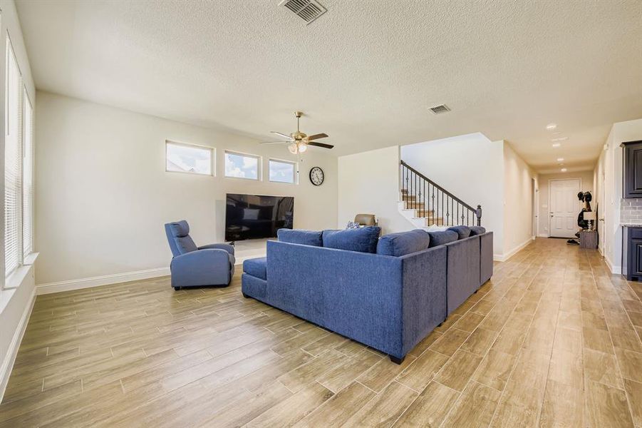Living area with light wood-style floors, stairway, a textured ceiling, and ceiling fan Living area with light wood-style floors, stairway, a textured ceiling, and ceiling fan