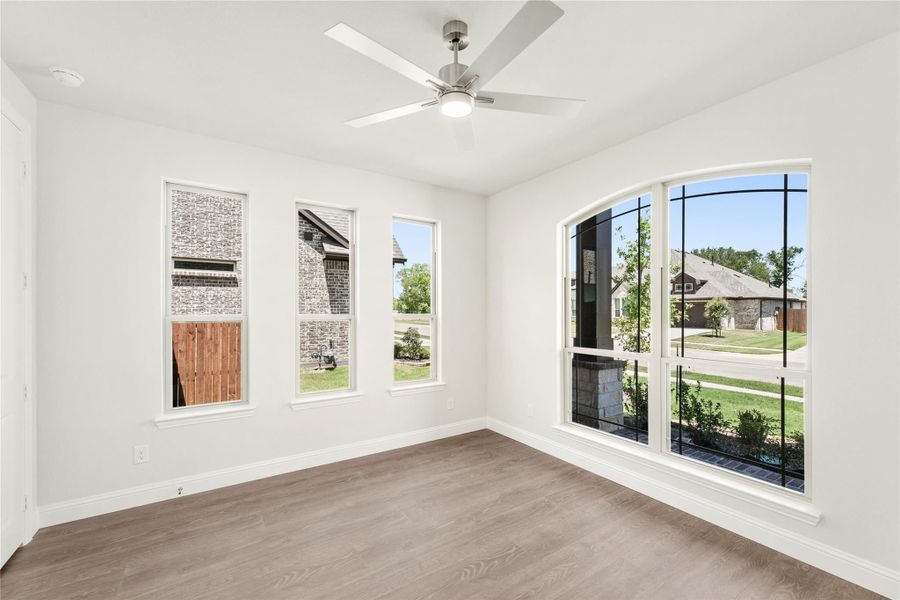 Empty room with hardwood floors, ceiling fan, and large arched windows overlooking a neighborhood