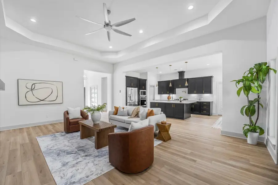 This photo showcases a spacious, modern open-concept living area with hardwood floors, a sleek kitchen featuring dark cabinetry and pendant lighting, and a comfortable seating area. The space is bright and inviting, with contemporary decor and a ceiling fan for comfort. This photo showcases a spacious, modern open-concept living area with hardwood floors, a sleek kitchen featuring dark cabinetry and pendant lighting, and a comfortable seating area. The space is bright and inviting, with contemporary decor and a ceiling fan for comfort.