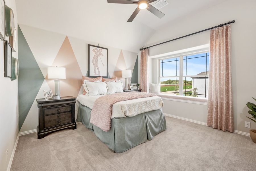 Bedroom with geometric accent wall, ceiling fan, carpet floors, and large window with outdoor view