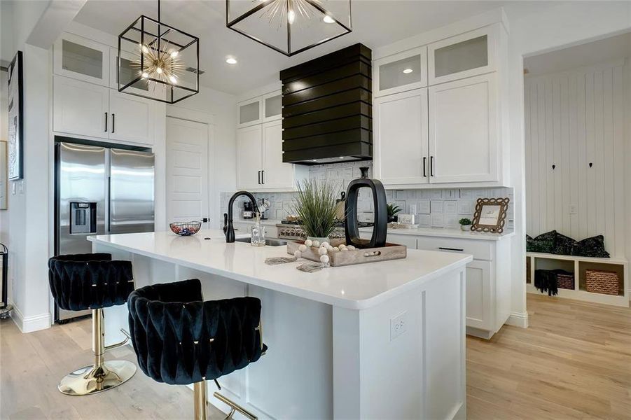 Kitchen with glass insert cabinets, a kitchen island with sink, stainless steel fridge with ice dispenser, light wood-style flooring, and recessed lighting