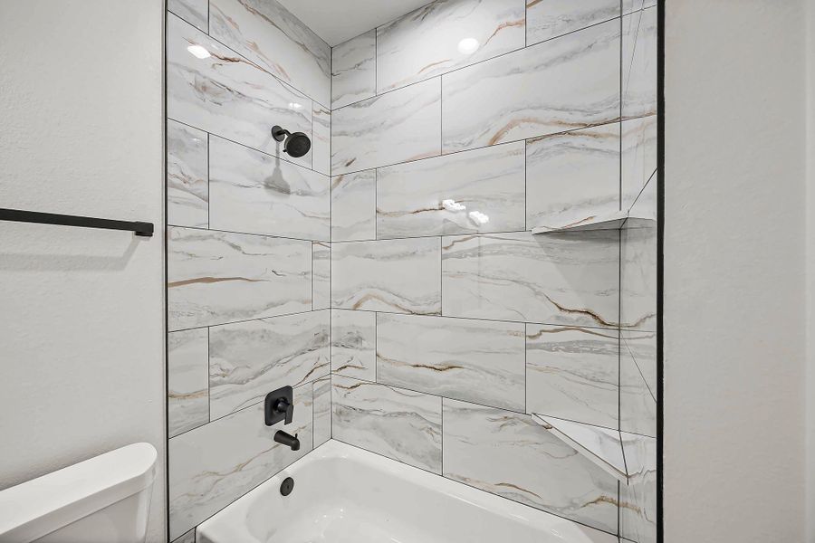 Luxurious bathroom featuring elegant marble-style tilework, a sleek black shower fixture, and a pristine white bathtub for a modern touch.