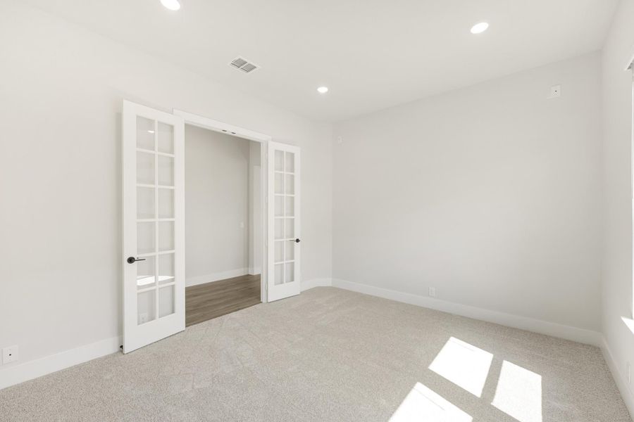 Empty room with carpet flooring, white walls, recessed lighting, and double French doors leading to an adjoining space