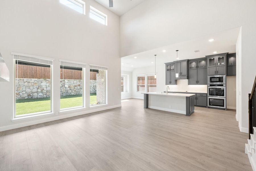 Open-concept living area with high ceilings, light wood floors, and kitchen with gray cabinets and center island