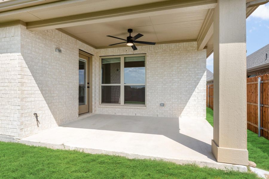 Covered back patio with ceiling fan, concrete floor, and white brick exterior wall
