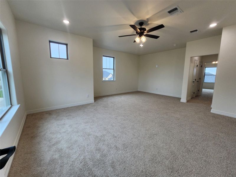 Spacious carpeted room featuring a ceiling fan with integrated lighting, multiple recessed lights, and several windows