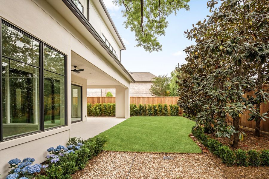 Another look at the thoughtfully landscaped grounds with wall of mature trees, clean hardscaping, and covered outdoor living extending from the home.