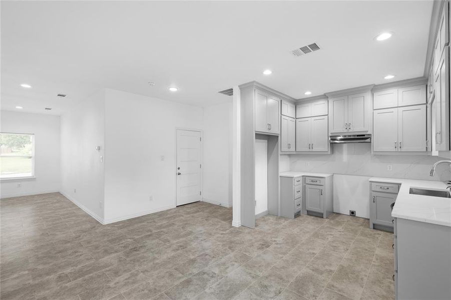 Kitchen featuring gray cabinetry, recessed lighting, light stone counters, backsplash, and under cabinet range hood Kitchen featuring gray cabinetry, recessed lighting, light stone counters, backsplash, and under cabinet range hood