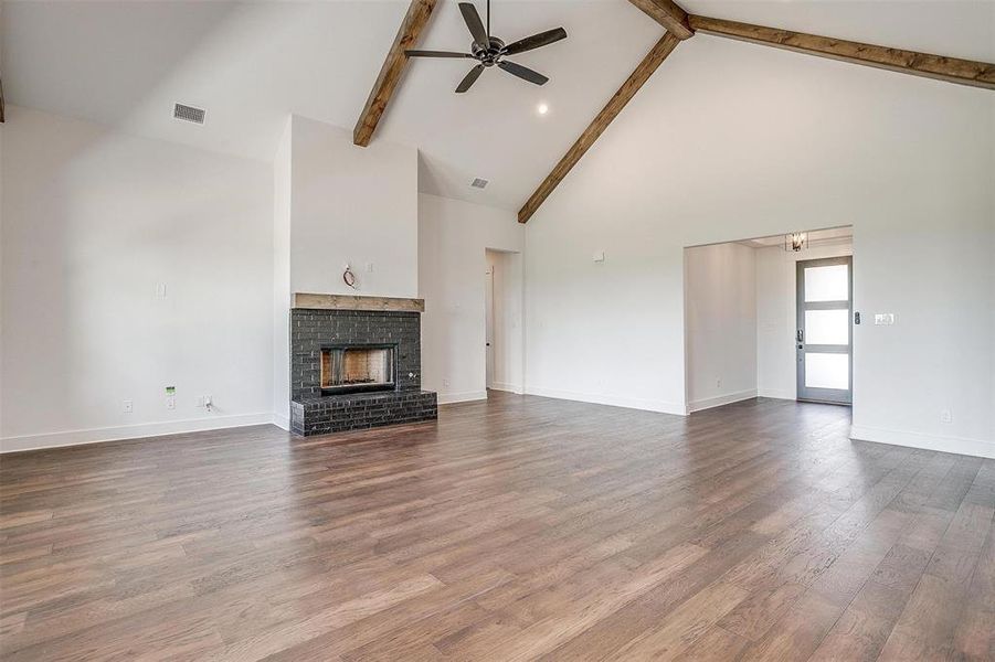 Unfurnished living room featuring beamed ceiling, a brick fireplace, hardwood / wood-style flooring, and high vaulted ceiling