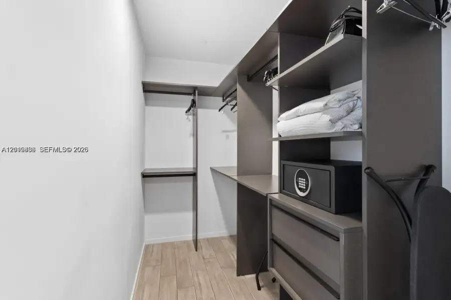 Custom closet system featuring dark wood-finish cabinetry, integrated shelving, hanging rods, and two soft-close drawers, complemented by wood-finish flooring Custom closet system featuring dark wood-finish cabinetry, integrated shelving, hanging rods, and two soft-close drawers, complemented by wood-finish flooring
