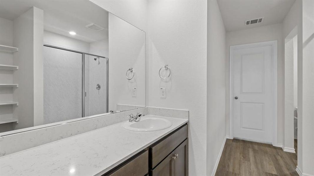 Bathroom featuring a single vanity with an integrated sink, a light-toned countertop, and dark wood-finish cabinetry Bathroom featuring a single vanity with an integrated sink, a light-toned countertop, and dark wood-finish cabinetry