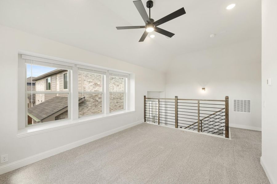 Open upstairs loft with carpet, ceiling fan, large windows, and metal railing overlooking lower floor