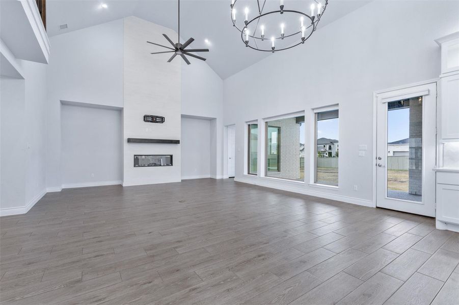Unfurnished living room with ceiling fan, a chandelier, high vaulted ceiling, wood tiled floors, and a large fireplace