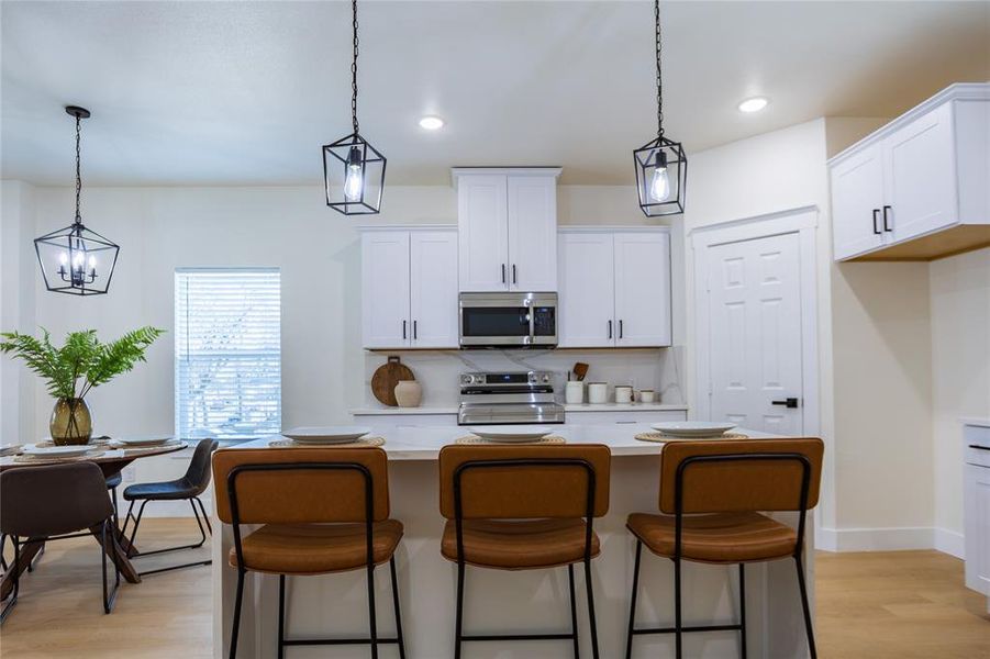 Kitchen with pendant lighting, appliances with stainless steel finishes, a kitchen island, white cabinetry, and recessed lighting