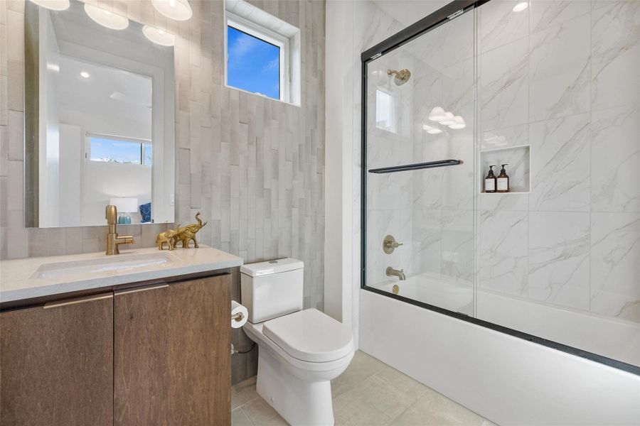 Full bathroom featuring vanity, healthy amount of natural light, enclosed tub / shower combo, tile walls, and light tile patterned flooring