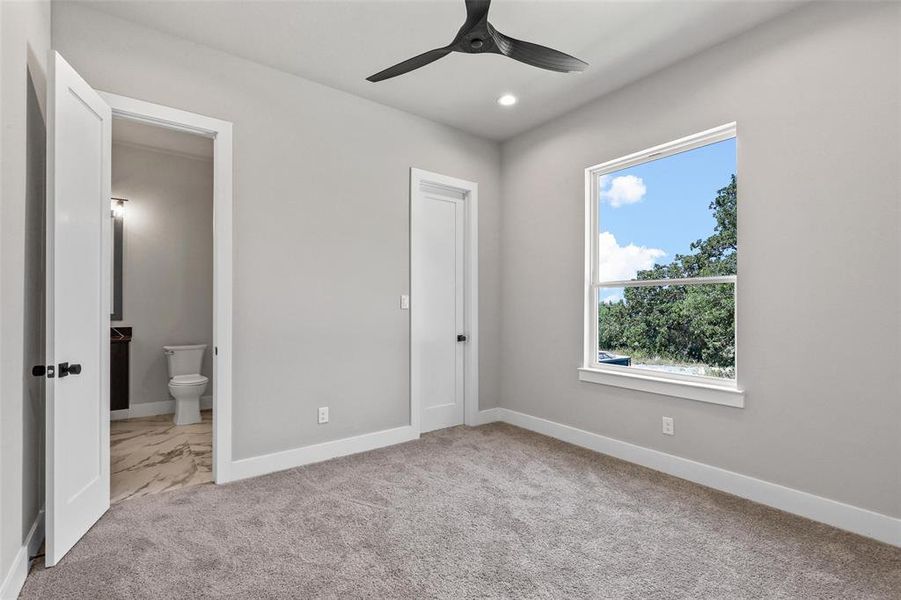 Unfurnished bedroom featuring ceiling fan, ensuite bath, and light carpet