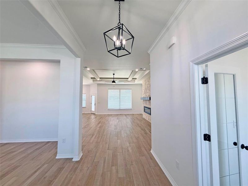Hall with light wood finished floors, a chandelier, a tray ceiling, and crown molding