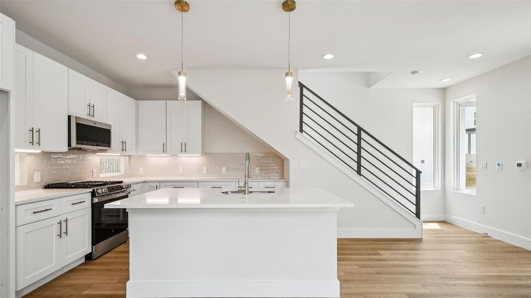 Kitchen with appliances with stainless steel finishes, decorative light fixtures, white cabinets, recessed lighting, and an island with sink Kitchen with appliances with stainless steel finishes, decorative light fixtures, white cabinets, recessed lighting, and an island with sink