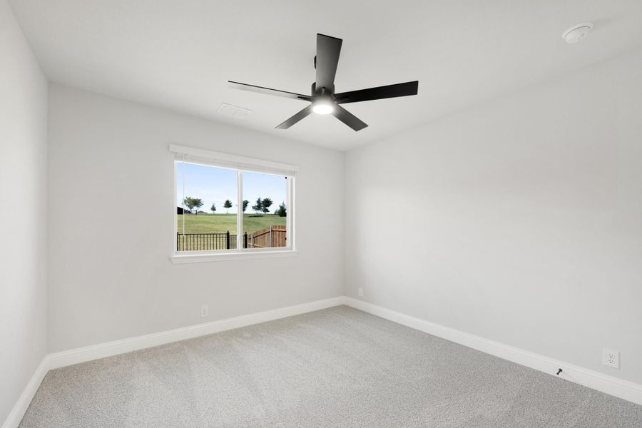 Empty bedroom with gray carpet, white walls, black ceiling fan, and a window with backyard view
