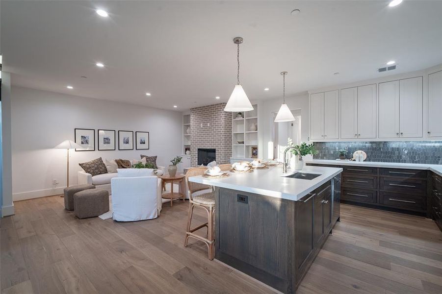 Kitchen featuring sink, an island with sink, a brick fireplace, white cabinets, and light hardwood / wood-style flooring