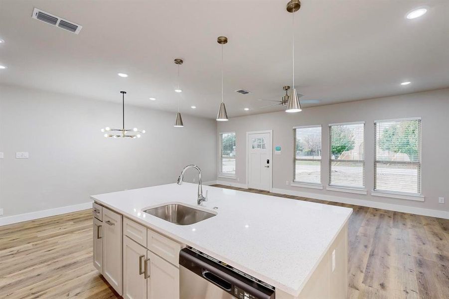 Kitchen with stainless steel dishwasher, a kitchen island with sink, sink, white cabinets, and hanging light fixtures