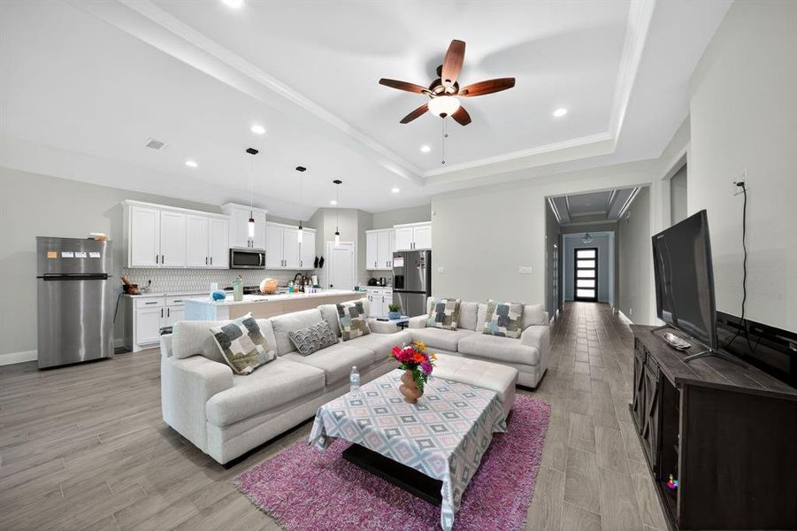 Living room with light wood-type flooring, ceiling fan, a tray ceiling, recessed lighting, and crown molding