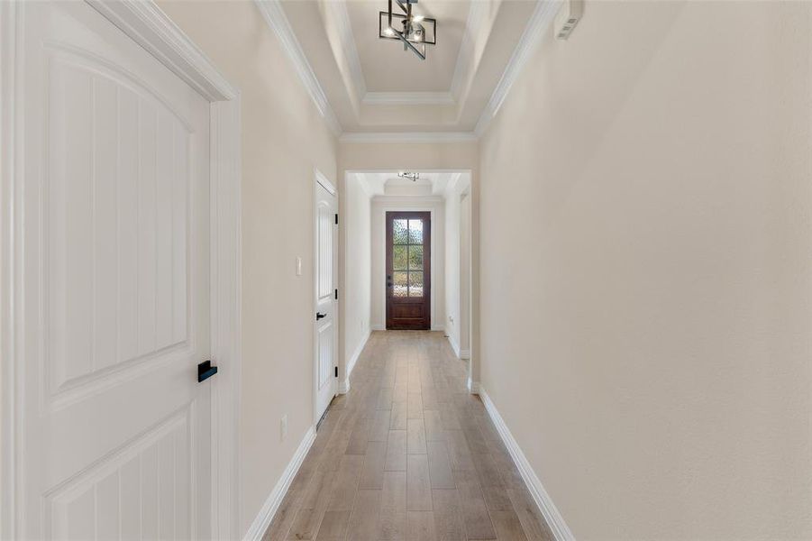 Corridor featuring crown molding, an inviting chandelier, a raised ceiling, and light hardwood / wood-style floors