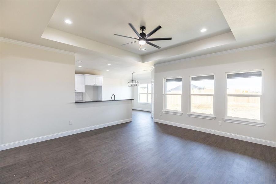 Spacious living area featuring wood-finish flooring, a tray ceiling with recessed lighting and a ceiling fan, and three large windows