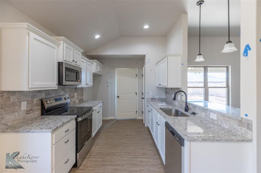 Kitchen with light stone countertops, appliances with stainless steel finishes, backsplash, white cabinetry, and vaulted ceiling